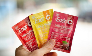 Holding Ener-C's flavour packets of Tangerine Grapefruit Vitamin C, Peach Mango Vitamin C, and Raspberry Vitamin C drink mix